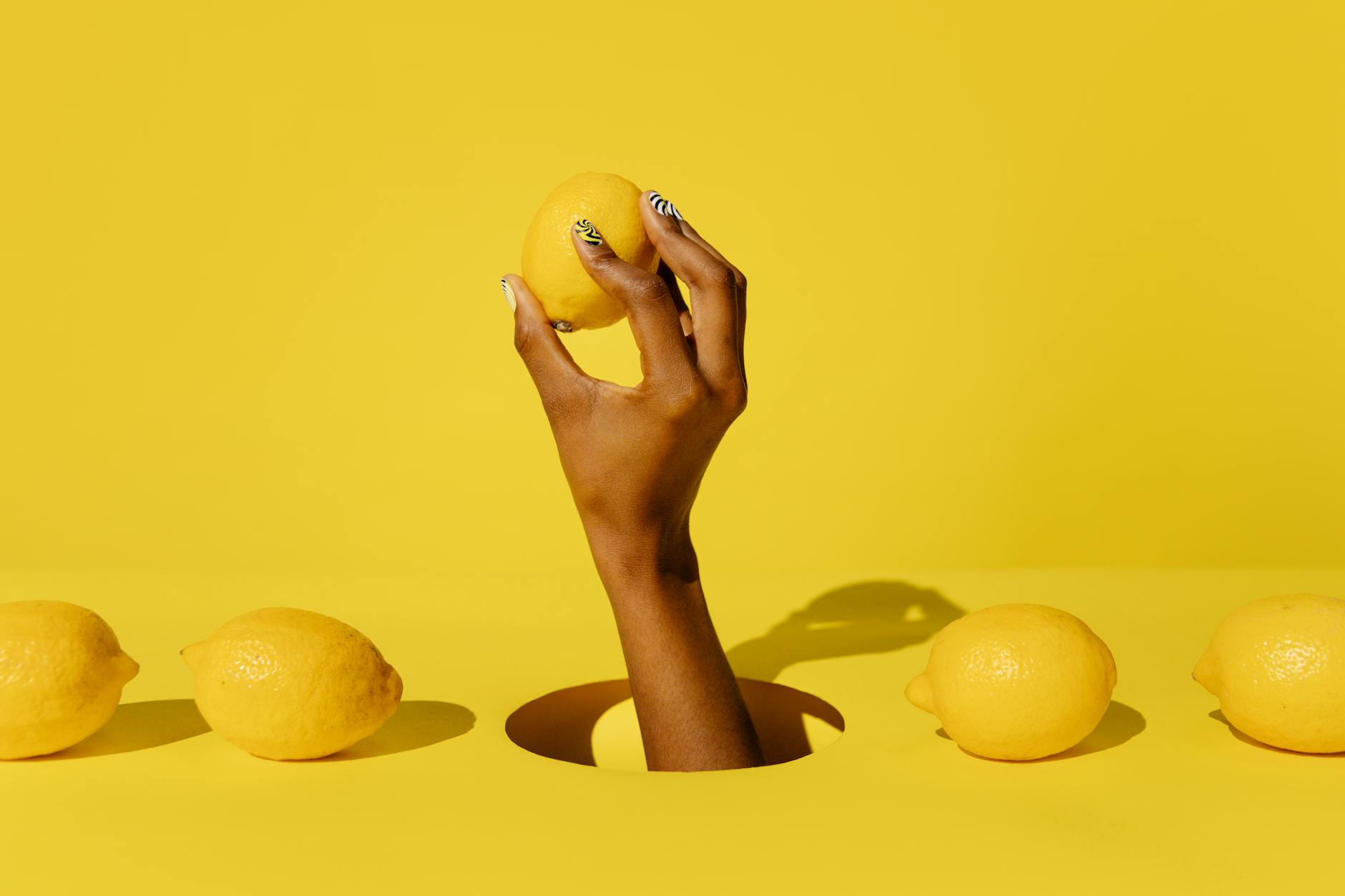 Hand holding a fresh lemon against a bright yellow background, symbolizing the Lemon vibrator and sexual self-care