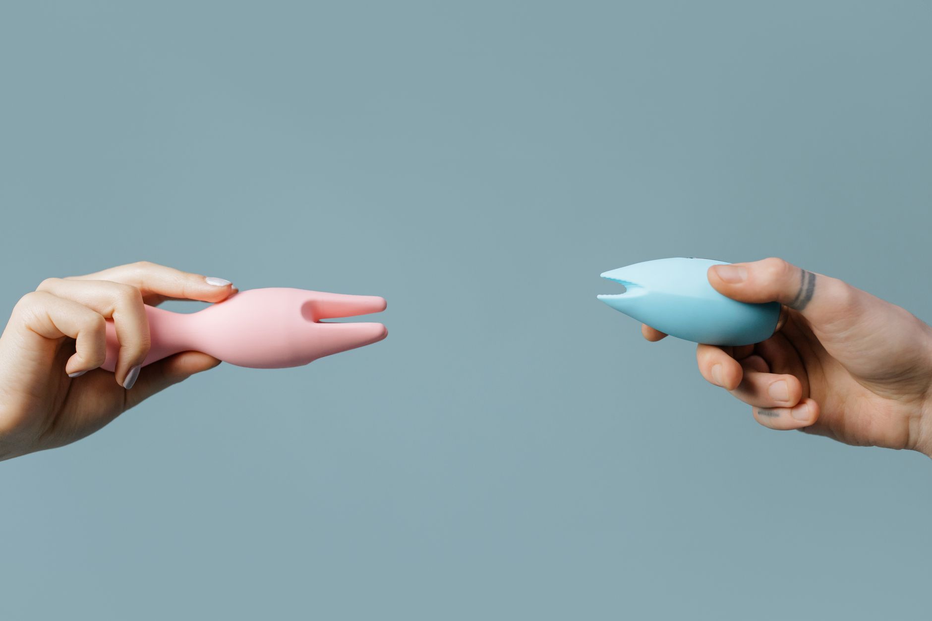 Two hands holding vibrators together, representing synchronized pleasure between partners