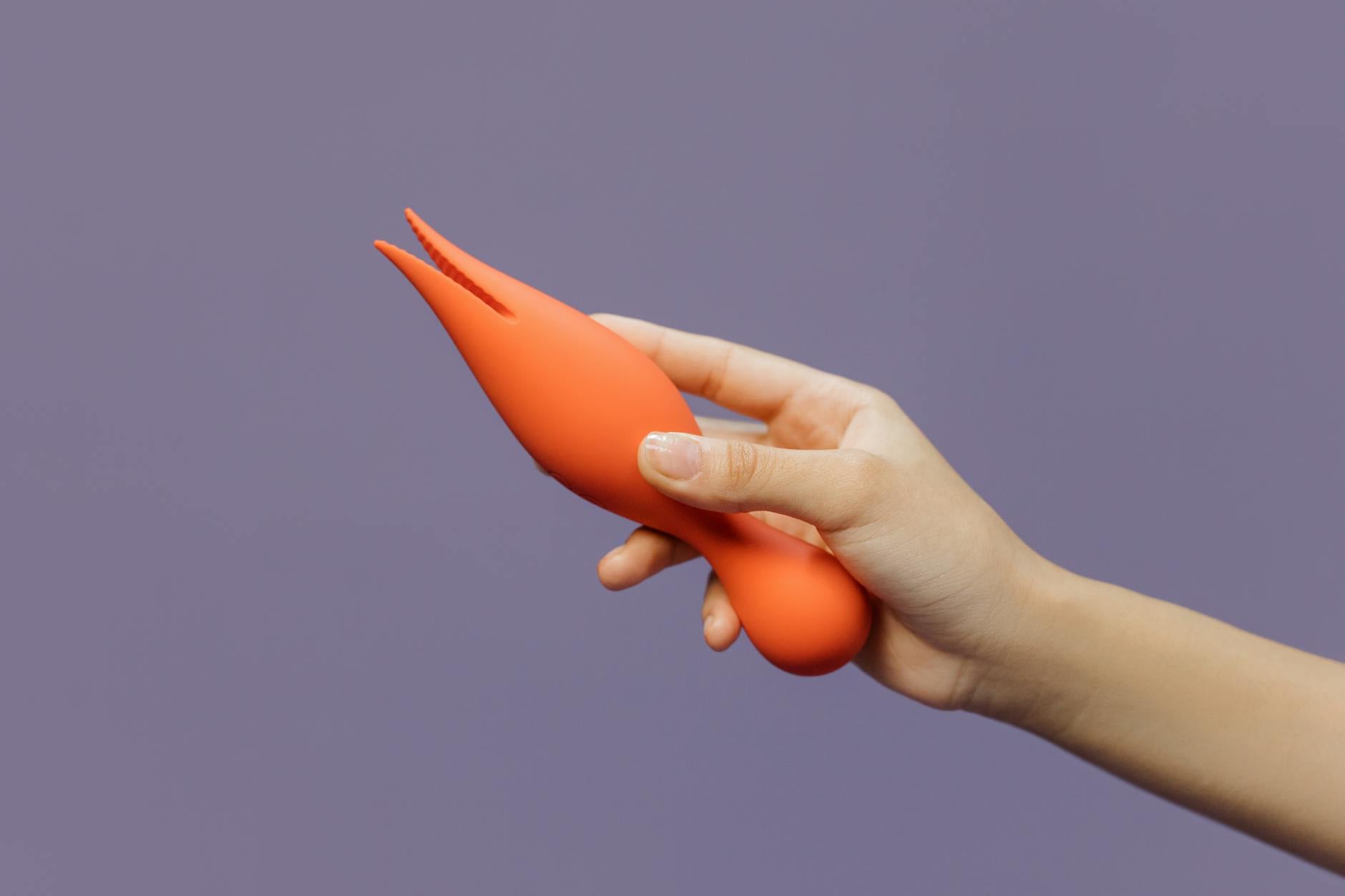 A hand holding a lemon-colored vibrator against a minimalist purple backdrop
