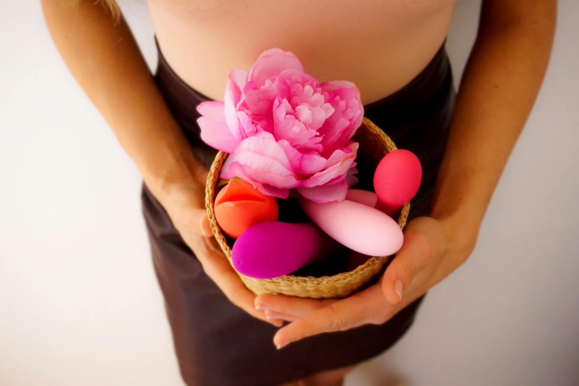 A basket of colorful vibrators and toys arranged with flowers, representing gentle postpartum self-care.
